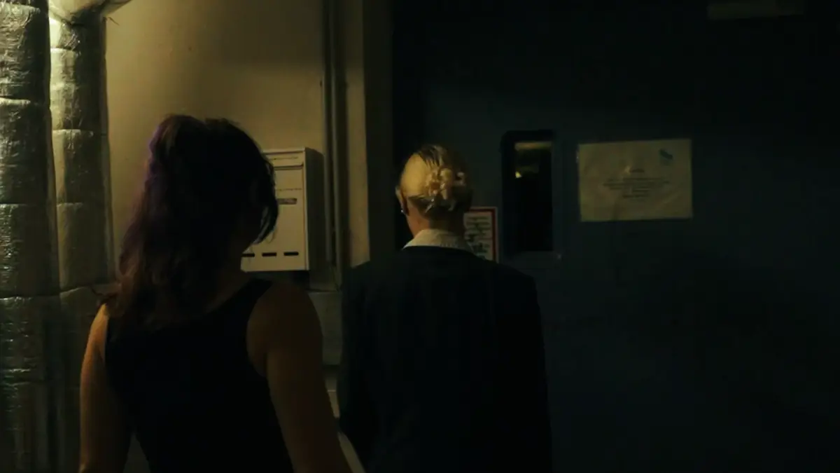 An agent in a suit and a player walk side by side down a basement corridor towards a steel door – still from a Secret Mission film