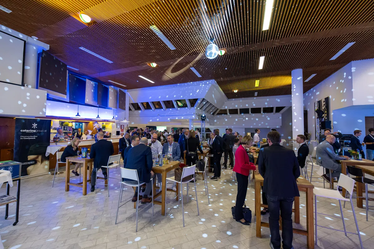 Abendstimmung im Foyer: Gäste an Stehtischen unter farbigem Licht