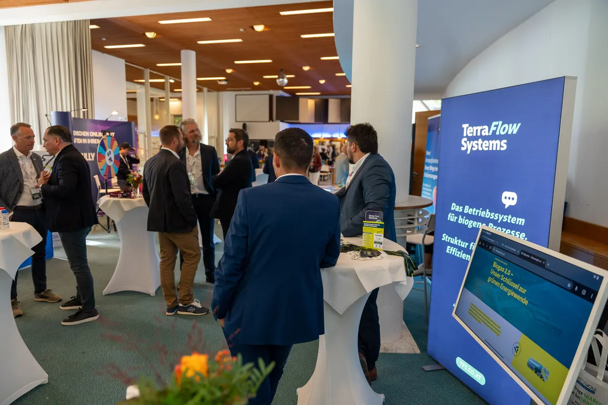 Gäste im Gespräch an Stehtischen im Foyer des Toscana Congress, dahinter Stände von Ausstellern