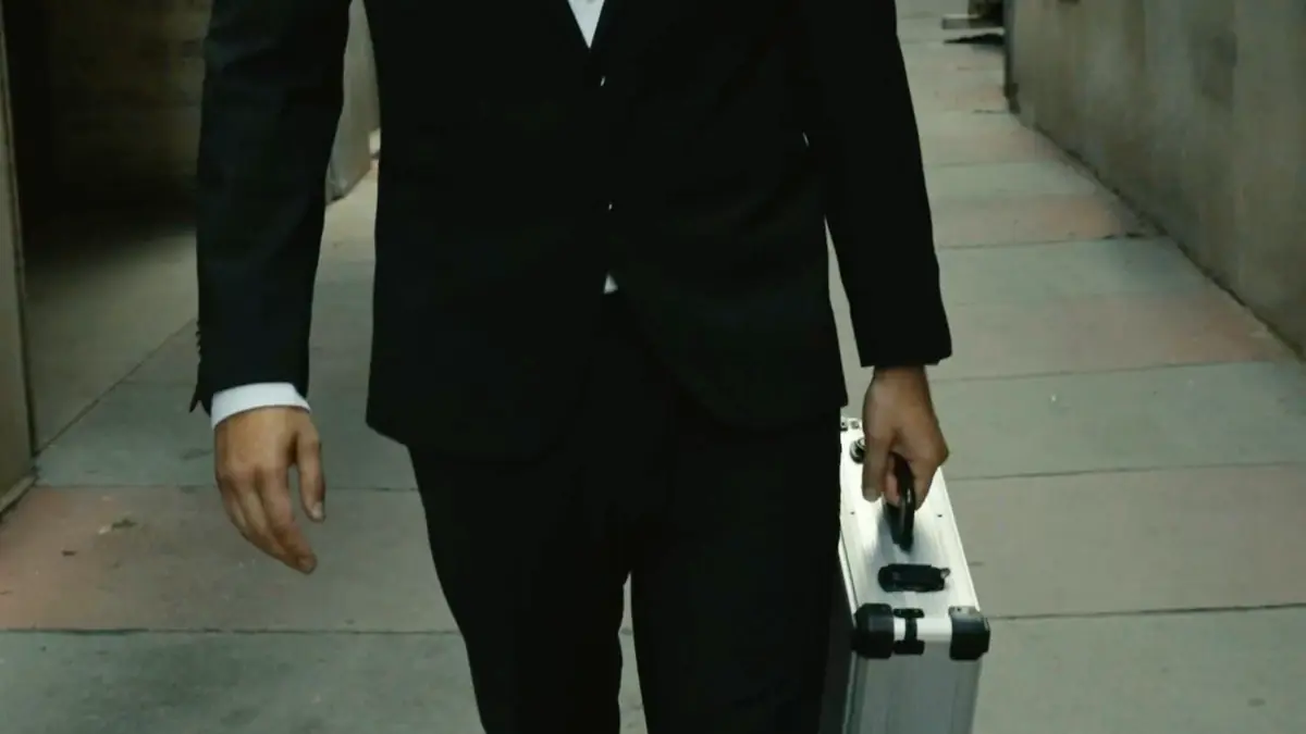 A man in a dark suit carries a silver case through a lane in Vienna’s old town
