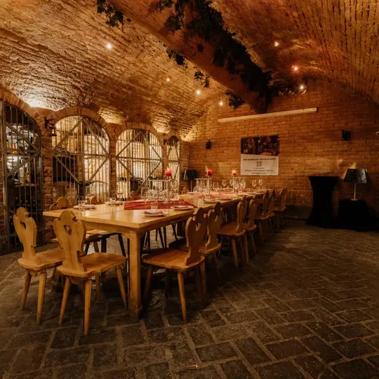 Lange Holztafel, festlich gedeckt, im beleuchteten Ziegelgewölbe des Weinbunkers