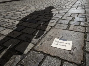 Zettel mit handschriftlichem Hinweis „Treffpunkt 14:00 – Café Central“ auf Wiener Kopfsteinpflaster, daneben der Schatten einer Person